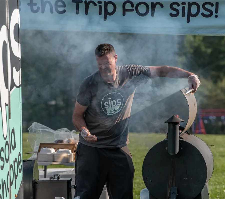 A food vendor working beside a smoking outdoor cooker in 2025