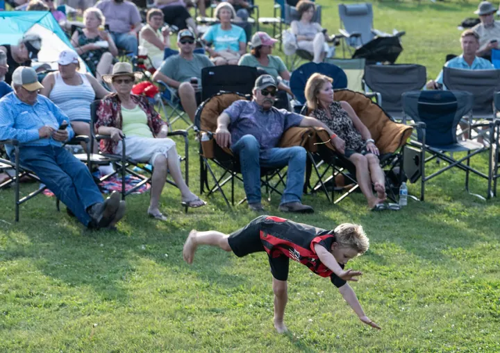 A child moving across the grass near a dog and festival crowd in 2025
