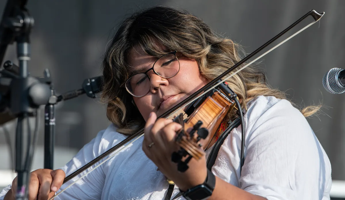 A violinist performing beneath the outdoor stage canopy in 2025